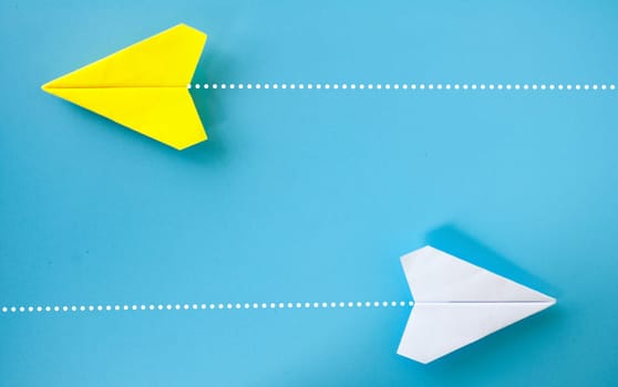 Top view of yellow and white paper airplane origami flying to a different direction on blue background.