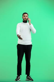 A man, full-length, on a green background, talking on the phone.