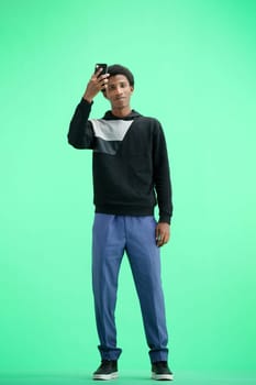 A man, full-length, on a green background, waving his phone.