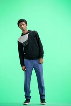 A man, full-length, on a green background, looks into the distance.