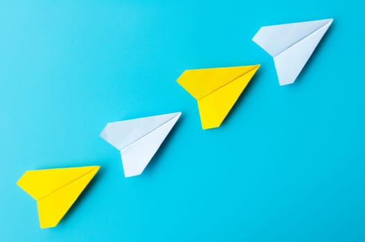 Top view of white and yellow paper airplanes origami flying on blue background.