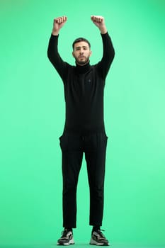 A man, full-length, on a green background, raised his hands up.