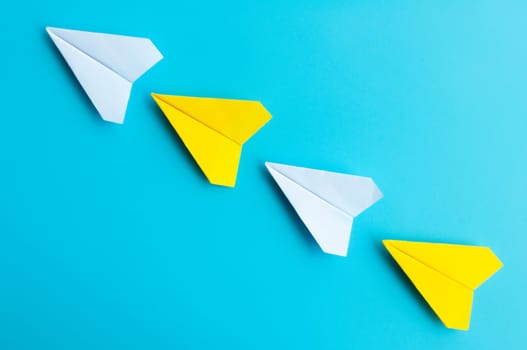 Top view of white and yellow paper airplanes origami flying on blue background