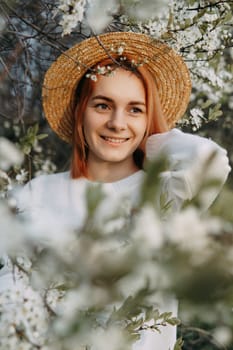 Portrait of a woman in a straw hat in a cherry blossom. Free outdoor recreation, spring blooming garden