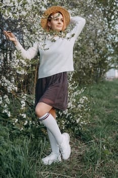 Portrait of a woman in a straw hat in a cherry blossom. Free outdoor recreation, spring blooming garden