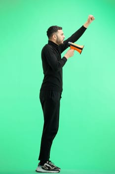 A man, full-length, on a green background, with a megaphone.