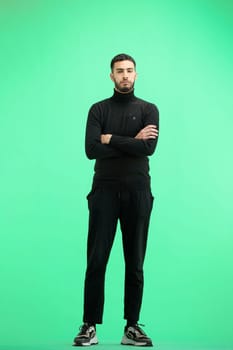 A man, full-length, on a green background, crossed his arms.