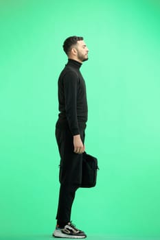 A man, full-length, on a green background, with a briefcase.