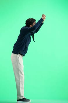 A man, full-length, on a green background, raised his hands up.