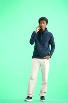A man, full-length, on a green background, talking on the phone.