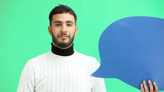 A man, close-up, on a green background, shows a blue comment sign.