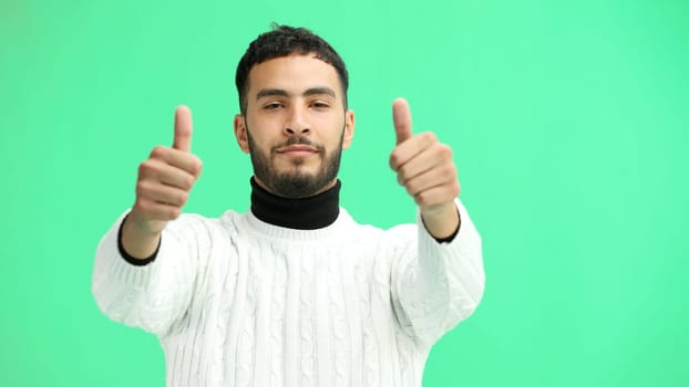 A man, close-up, on a green background, shows his thumbs up.