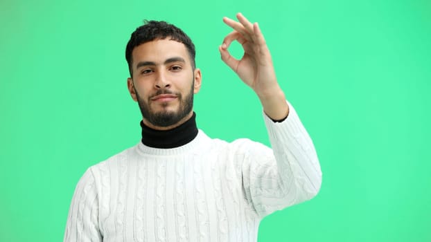 A man, close-up, on a green background, shows an ok sign.