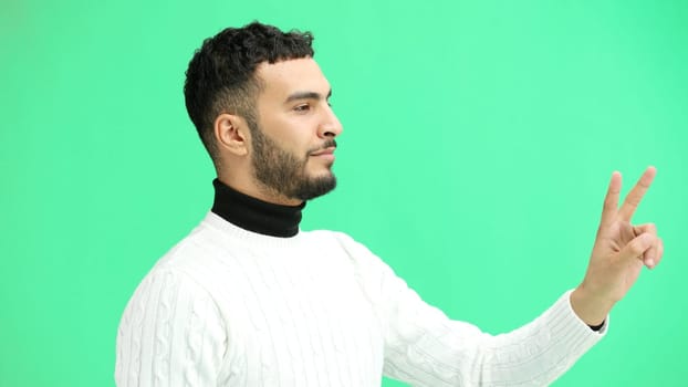 A man, close-up, on a green background, shows a victory sign.