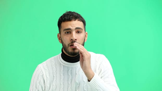 A man, close-up, on a green background, tells a secret.
