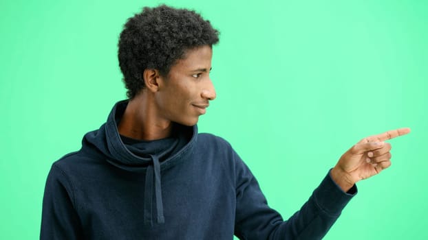 A man, close-up, on a green background, points to the side.