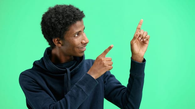 A man, close-up, on a green background, points to the side.