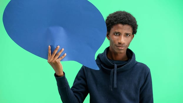 A man, close-up, on a green background, shows a blue comment sign.