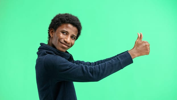 A man, close-up, on a green background, shows his thumbs up.