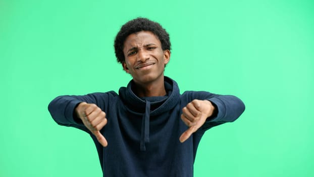 A man, close-up, on a green background, shows his thumbs down.