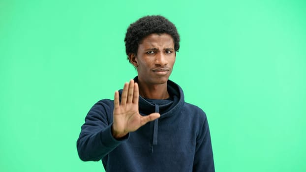 A man, close-up, on a green background, shows a stop sign.