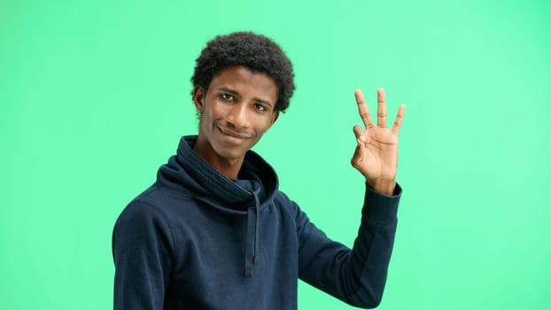 A man, close-up, on a green background, shows an ok sign.