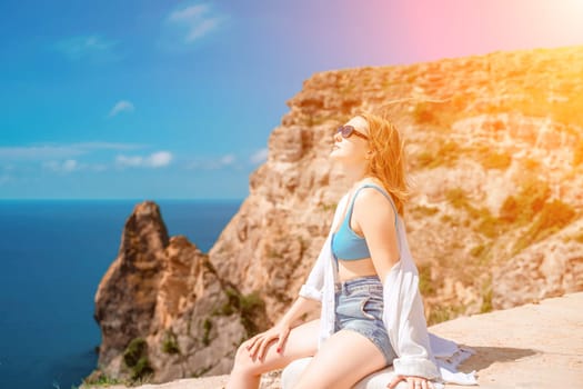 Woman travel summer sea. Portrait of a happy woman on a background of rocks and the sea. Side view of a woman in a white shirt and swimsuit. Freedom and happiness.