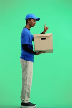 The deliveryman, in full height, on a green background, with a box, shows an important sign.