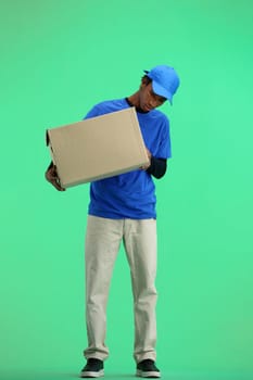 The deliveryman, in full height, on a green background, examines the box.