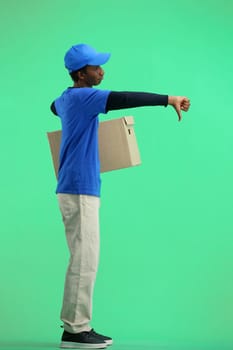 The deliveryman, in full height, on a green background, with a box, shows his finger down.