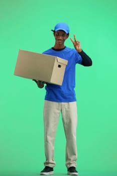 The deliveryman, in full height, on a green background, with a box, shows a victory sign.
