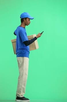 The deliveryman, in full height, on a green background, with a box, talking on the phone.