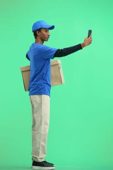 The deliveryman, in full height, on a green background, with a box, talking on the phone.