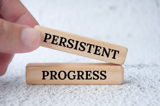 Hand holding wooden blocks with text, persistent progress. Operational excellence concept.