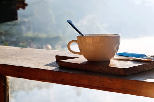 Coffee cup on wooden table with morning fog and mountain background