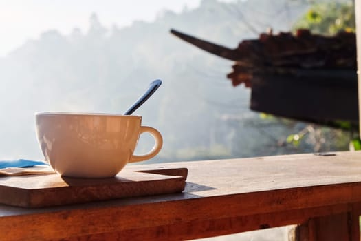 Coffee cup on wooden table with morning fog and mountain background