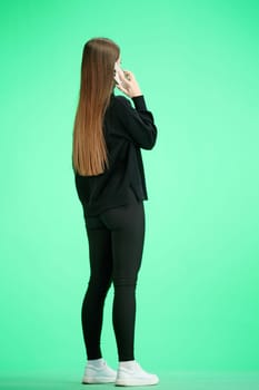 A woman, full-length, on a green background, talking on the phone.