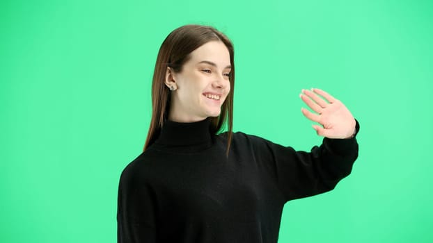 A woman, close-up, on a green background, waving her hand.
