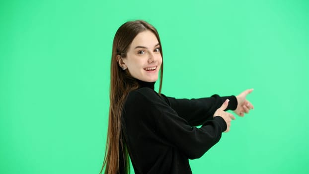 A woman, close-up, on a green background, points forward.