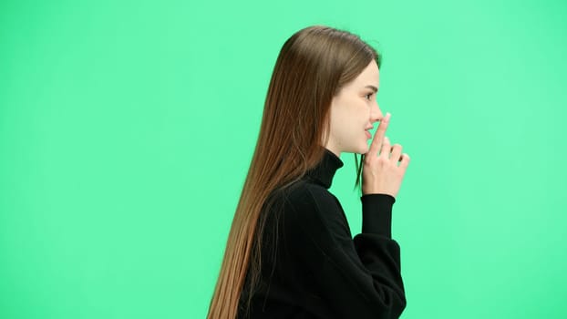 A woman, close-up, on a green background, shows a sign of silence.