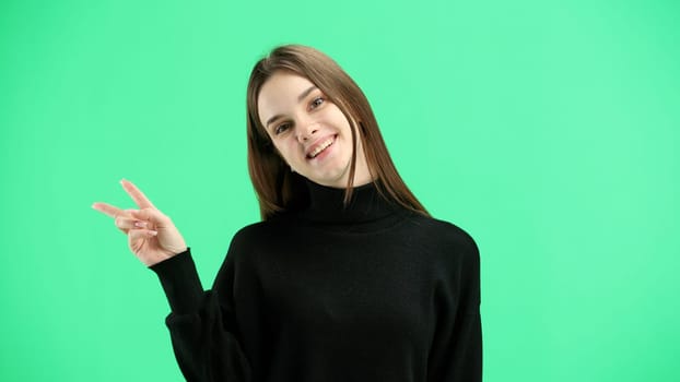 A woman, close-up, on a green background, shows a victory sign.