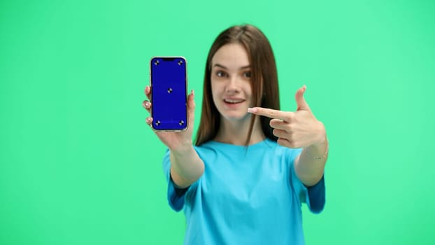 A woman, close-up, on a green background, shows a phone.