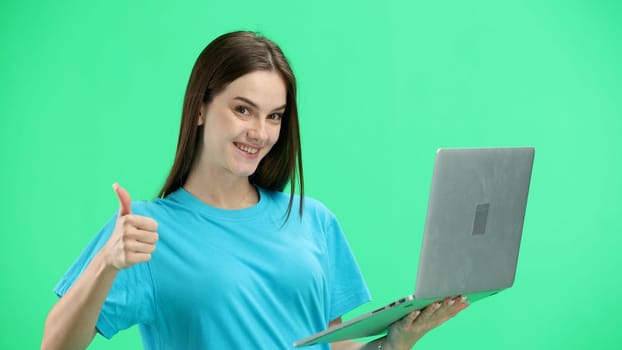 A woman, close-up, on a green background, uses a laptop.