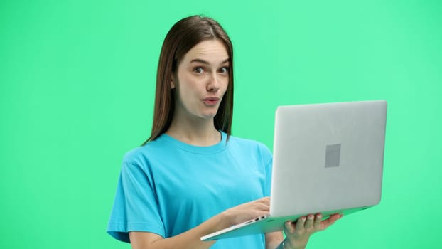 A woman, close-up, on a green background, uses a laptop.