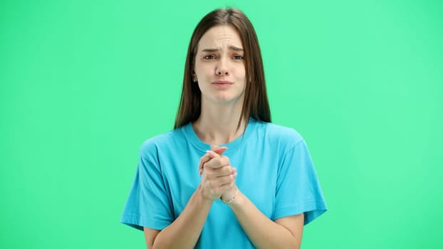 A woman, close-up, on a green background, pleads.