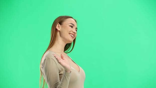 A woman, close-up, on a green background, waving her hand.