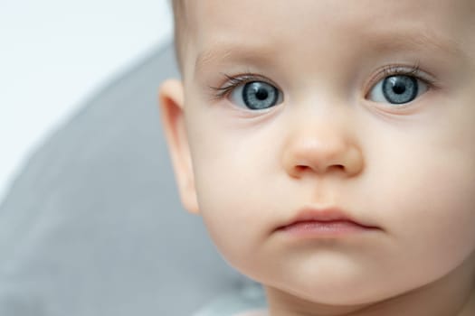 A close up of a babys face with blue eyes, rosy cheeks, and long eyelashes, looking directly at the camera with a neutral expression