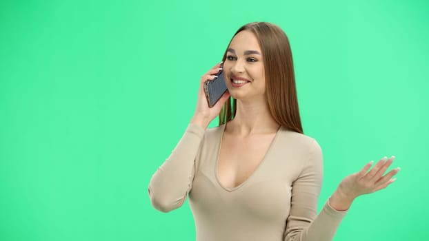 A woman, close-up, on a green background, talking on the phone.