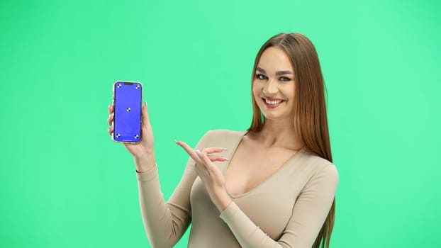 A woman, close-up, on a green background, shows a phone.