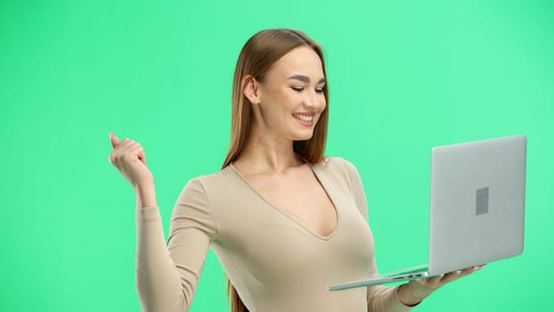 A woman, close-up, on a green background, uses a laptop.